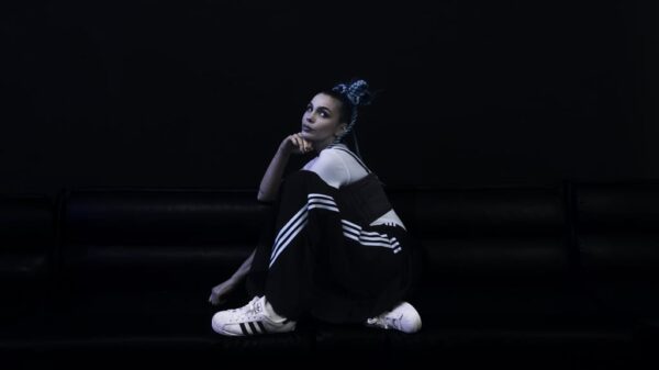 Rose Villain seduta su divano nero indossa il completo Firebird e le adidas Superstar nella campagna SS25