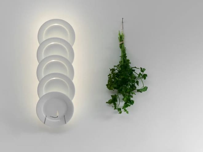 Lampada da cucina composta da cinque piatti in porcellana illuminati da un LED nascosto. Disposizione flessibile ed espandibile. Un fiammifero disegnato si “accende” con la luce: un’illusione giocosa.