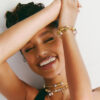 Tyla sorride mostrando i bracciali Pandora con charm dorati, anelli e collane sovrapposte